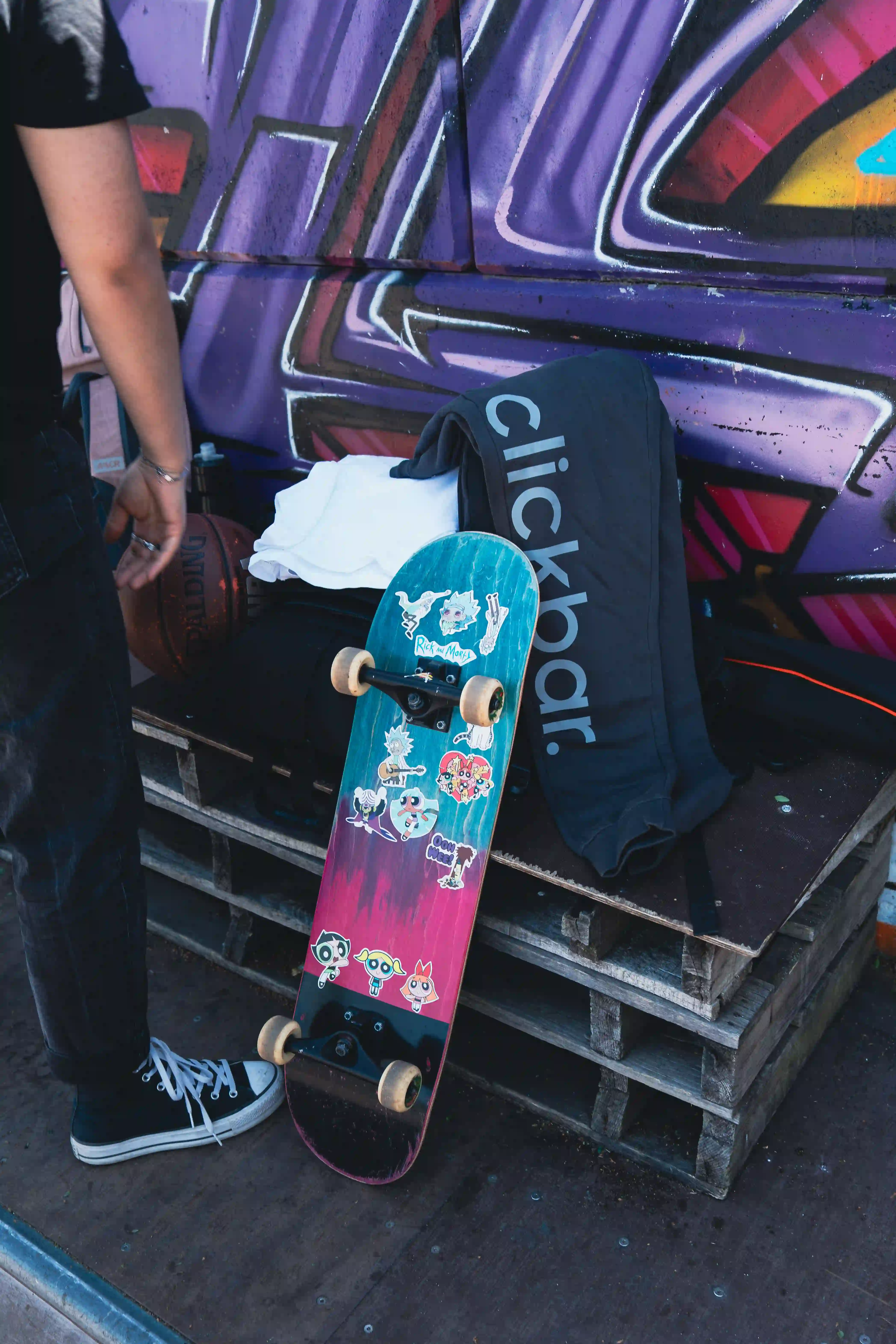 Jogginghose mit 'clickbar.' Logo auf Paletten neben buntem Skateboard.